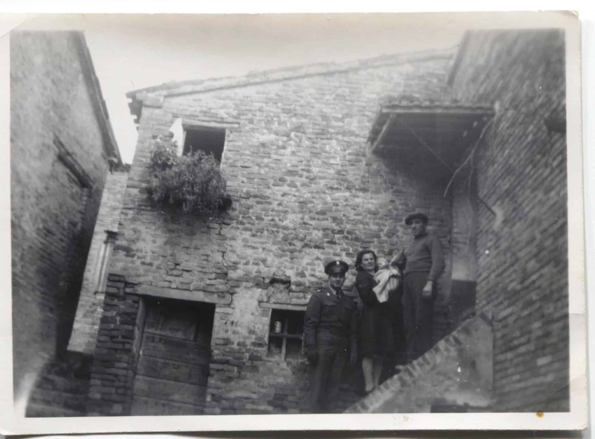Image of an old stone house where four members of the Talevi stand outside on a staircase.