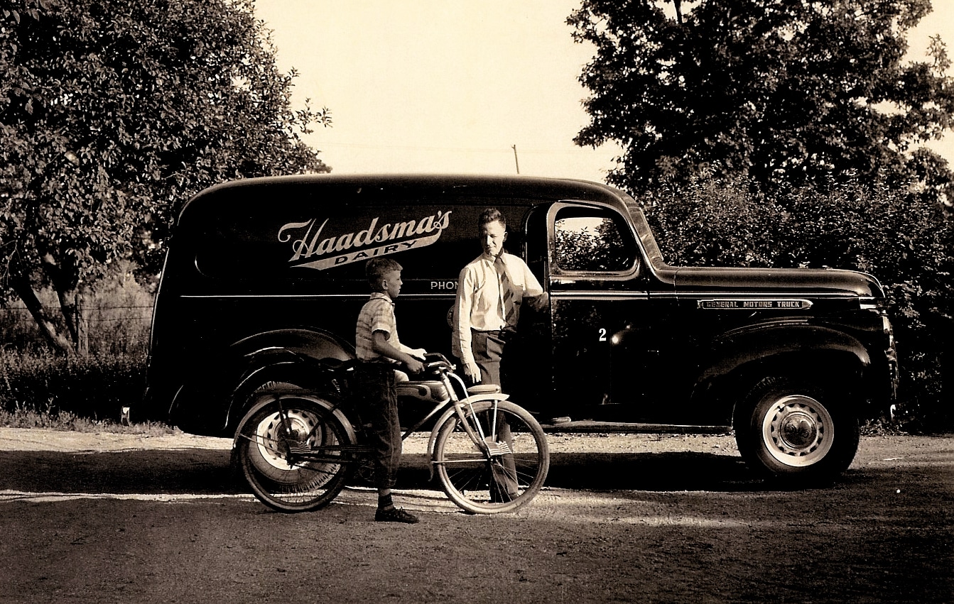 Man standing by the Haadsma Dairy truck, a boy in a bicycle has stopped to talk to him