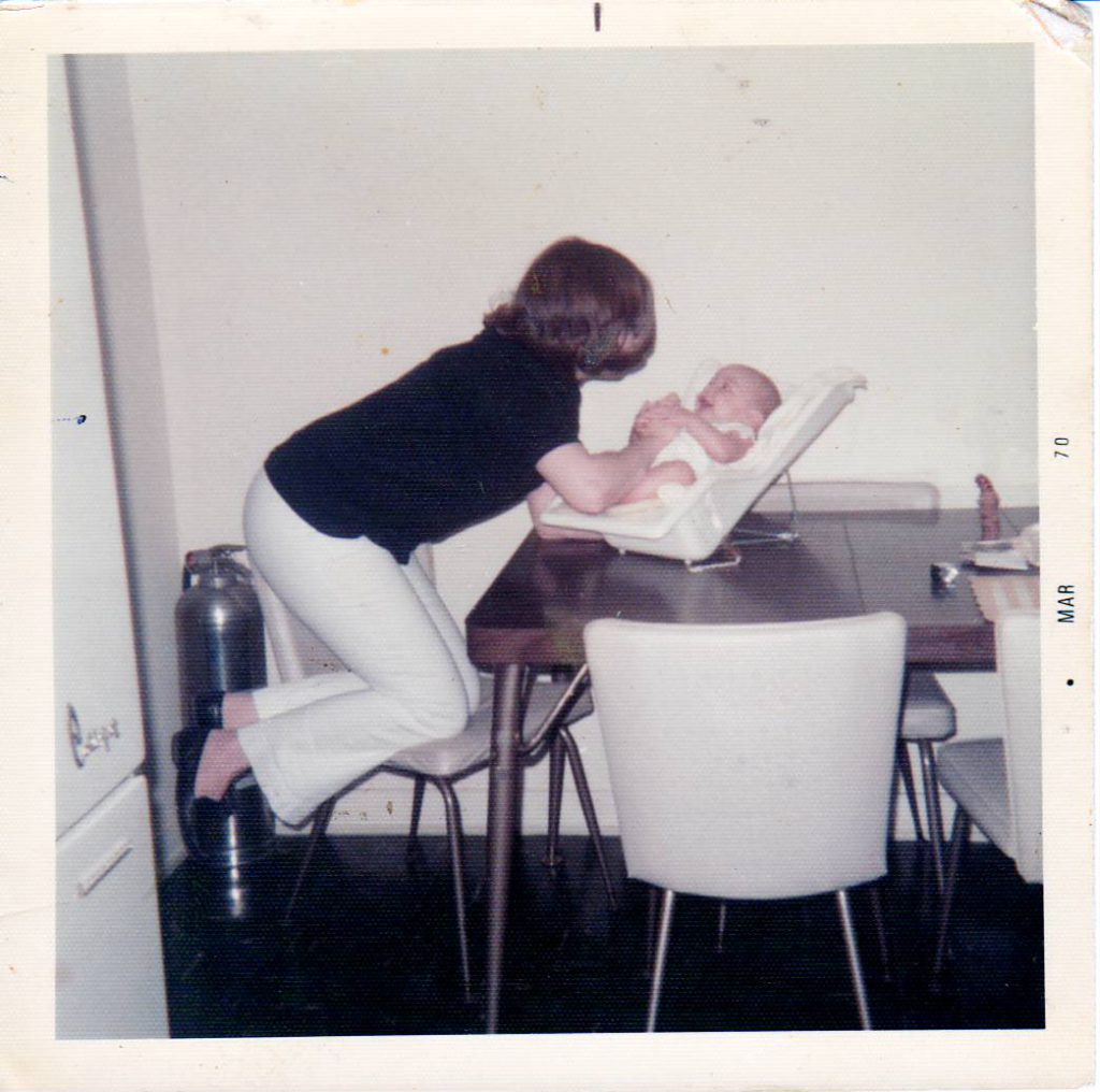 Susie leaning over and caring for her baby who is placed in a seat on top of the table
