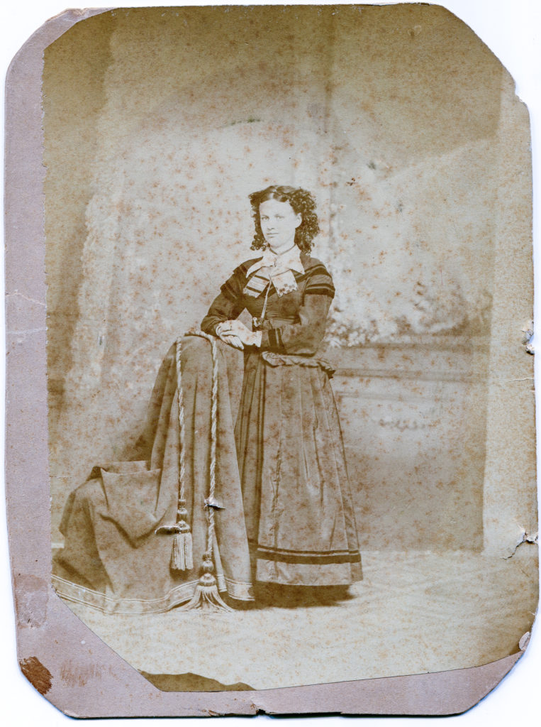 Sepia photo of a woman in an 1870s-style dress.